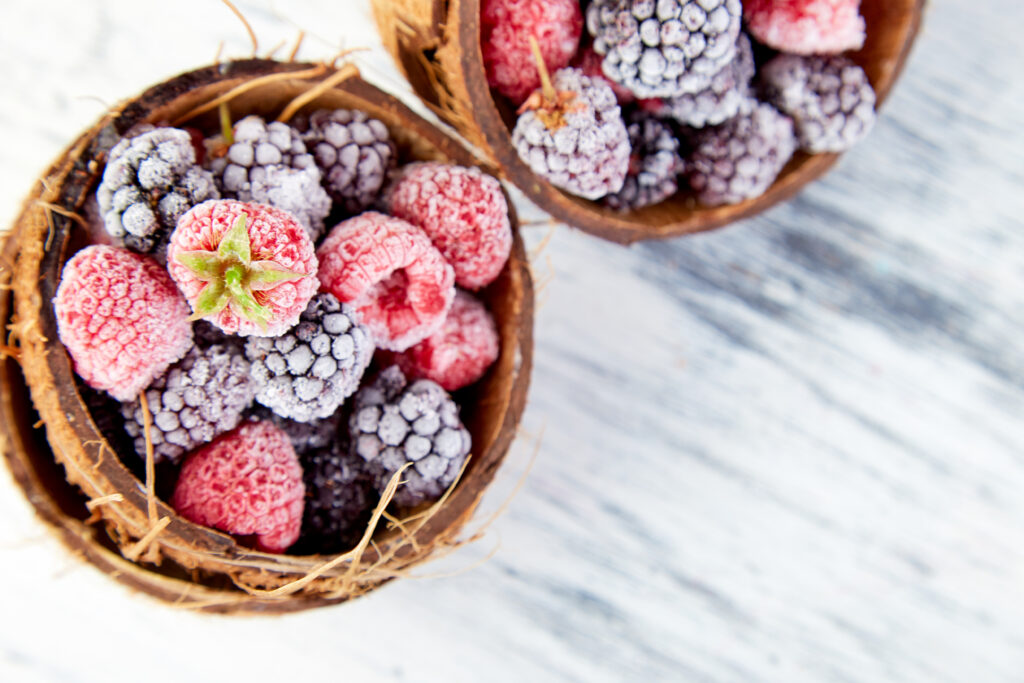Frozen black and red raspberries in coconut bowl.